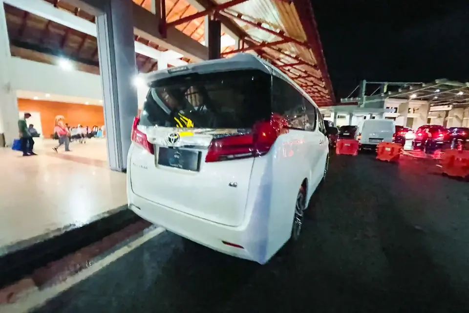 White Toyota Alphard with the tailgate open at the Ngurah Rai airport pickup lane