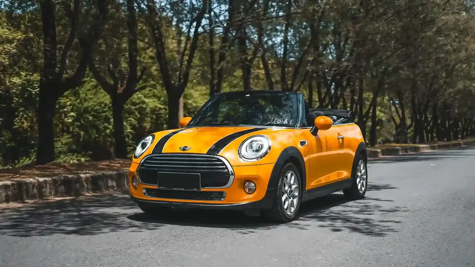 Orange Mini Cooper convertible on a tree-lined road